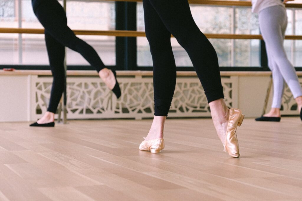 The legs of three adult ballet dance students at an indoor ballet dance studio