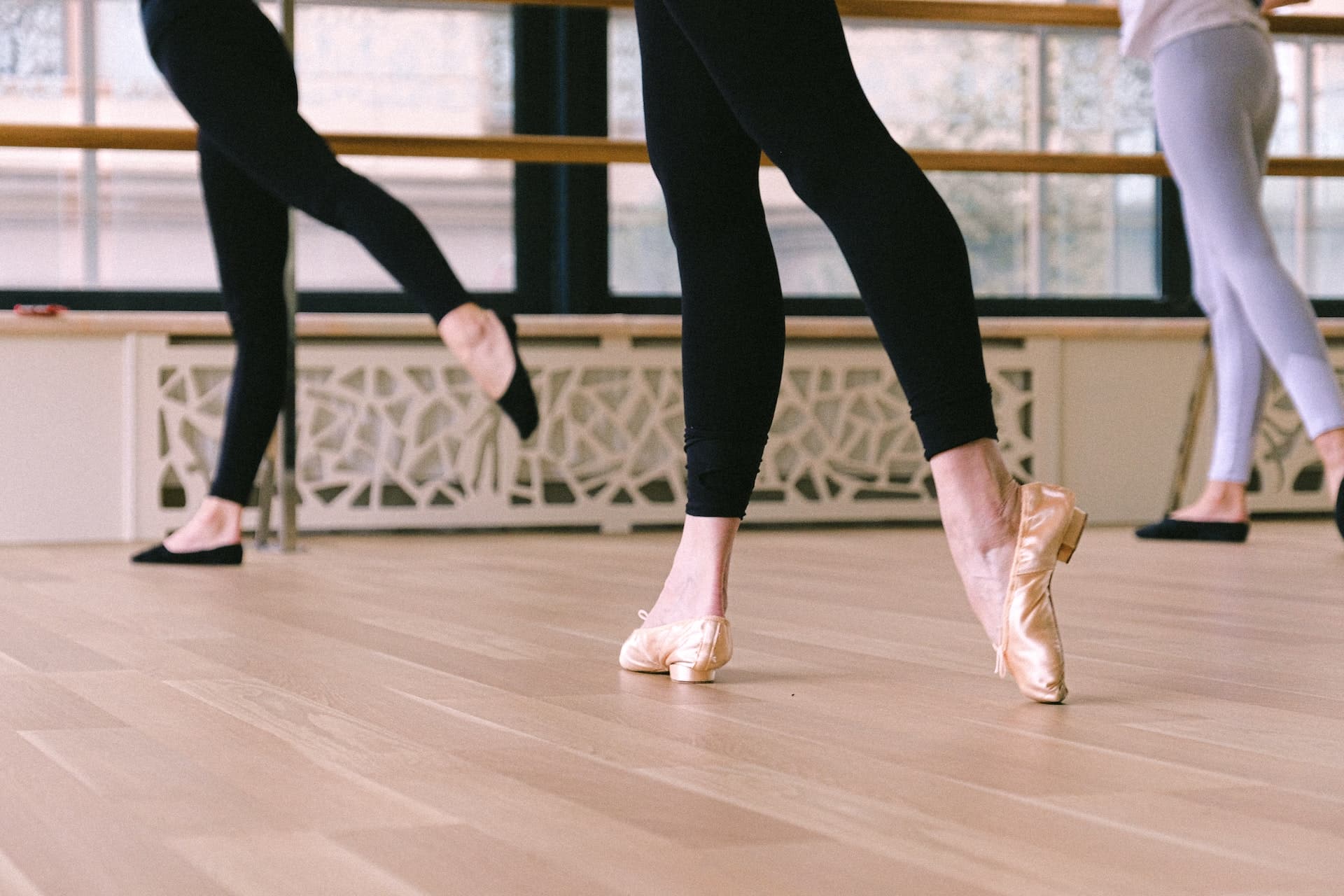 The legs of three adult ballet dance students at an indoor ballet dance studio