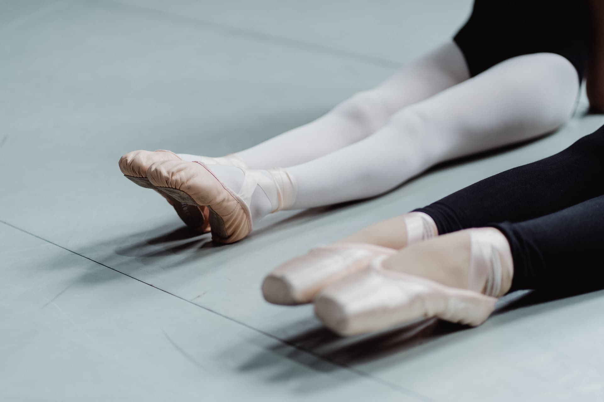 the legs of two girl ballet dancers in peach colored ballet shoes, one girls is wearing black leggings and the other has white tights