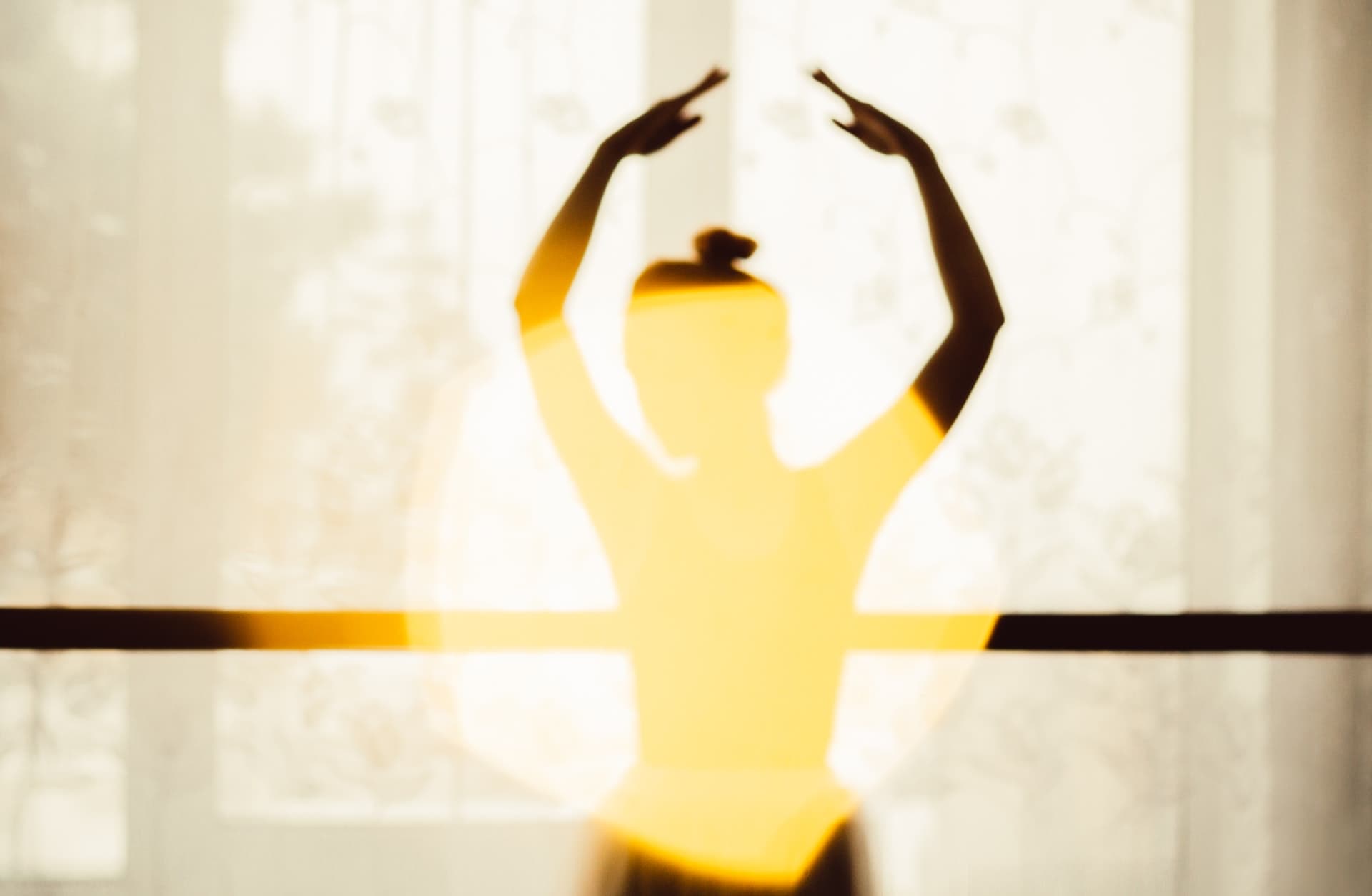 the silhouette of the upper body younger female ballet dancer who is standing in front of a window in the ballet dance studio