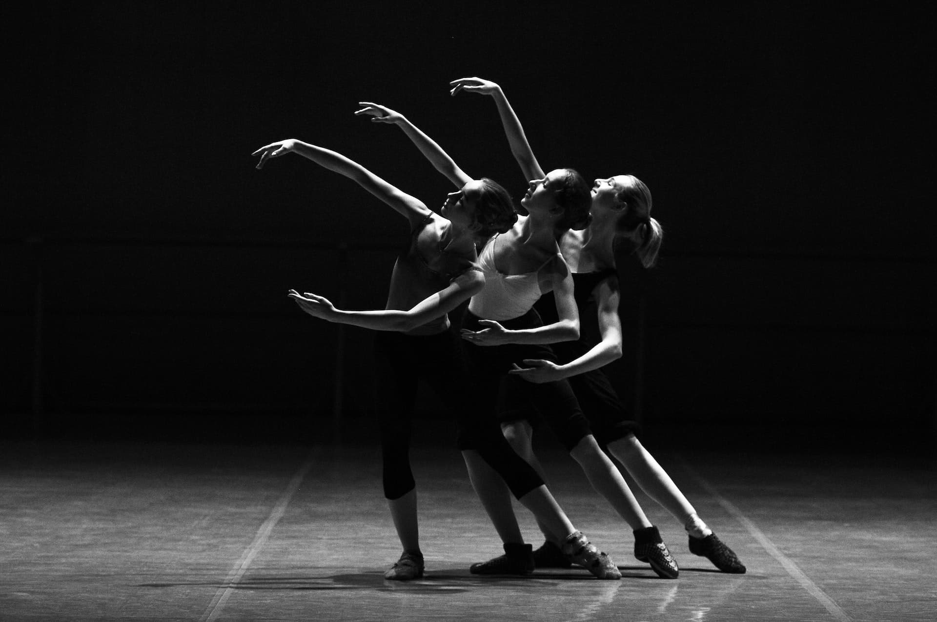 A dramatic black and white photo of three young female ballet dancers performing on stage
