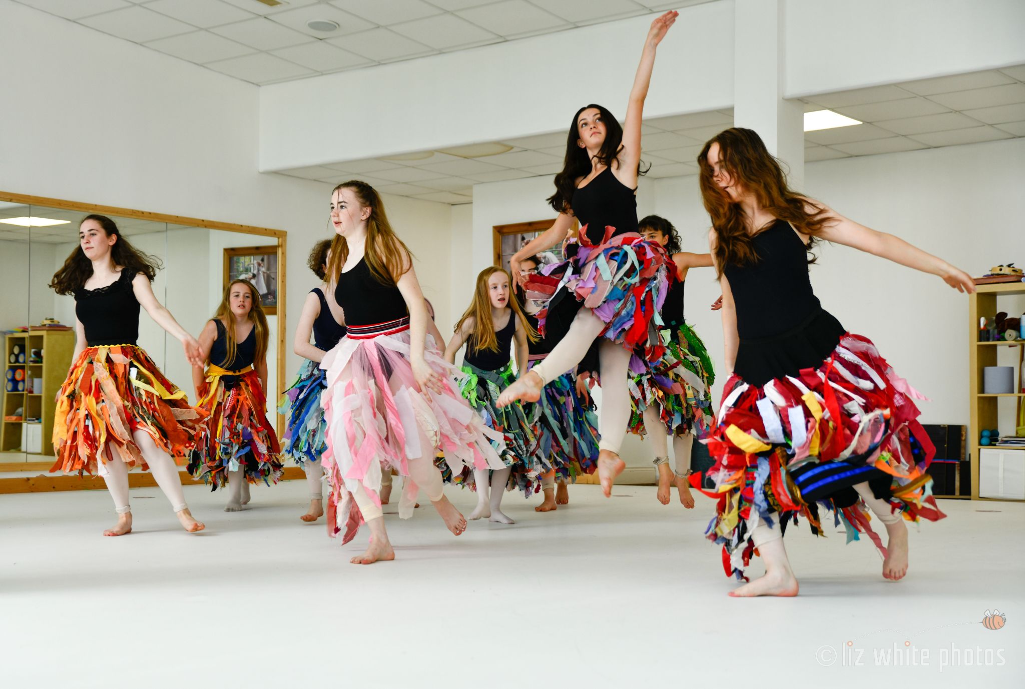 ten teenage students of Ruth Shine School of Dance are practicing ballet in a Dublin dance studio. Their dresses are very colourful except for their tops which are black