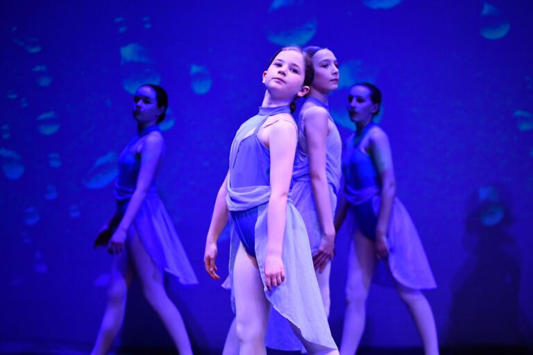 A young female ballet and contemporary dance student in a blue dance clothing performs on stage for parents at a Ruth Shine School of Dance performance night in Dublin