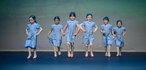 photo of a group of six junior age ballet dancers performing on a stage at a ballet dance performance for a ballet school
