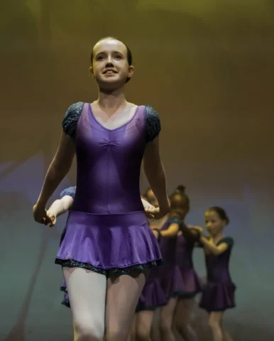 photo of a young girl in purple leotard leading a group of other mid-level ballet dancers at a ballet dance performance for parents